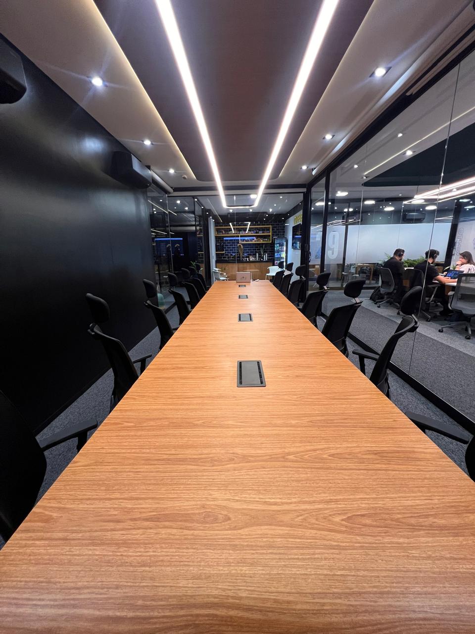 Sala de reunião do Next90 com mesa de madeira, janelas e plantas